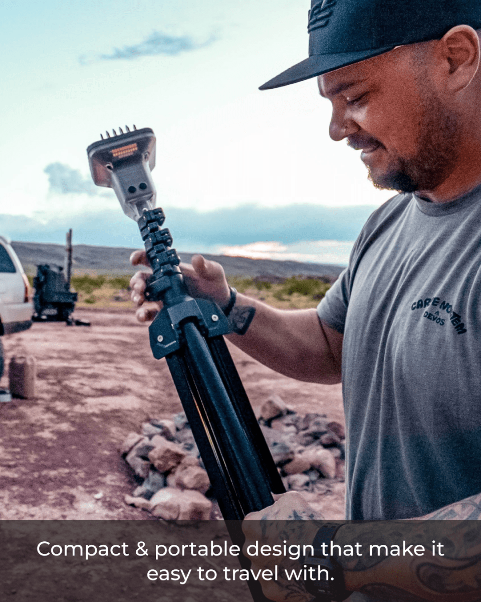 A man is holding a compact, telescoping LED lantern while standing outdoors, with a rocky landscape and a vehicle in the background. The lantern features a modern design, showcasing its portability and ease of use for outdoor activities.